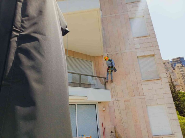 עובד מבצע עבודות סנפלינג בגובה על חזית מבנה לצורך תיקונים ותחזוקת קירות חוץ.