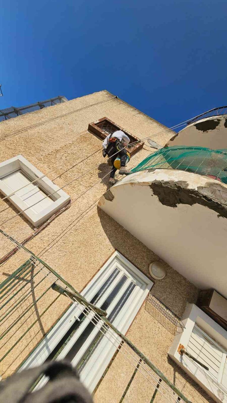 עובד מבצע עבודת סנפלינג בגובה על גג מבנה לצורך תיקונים ותחזוקה חיצונית.