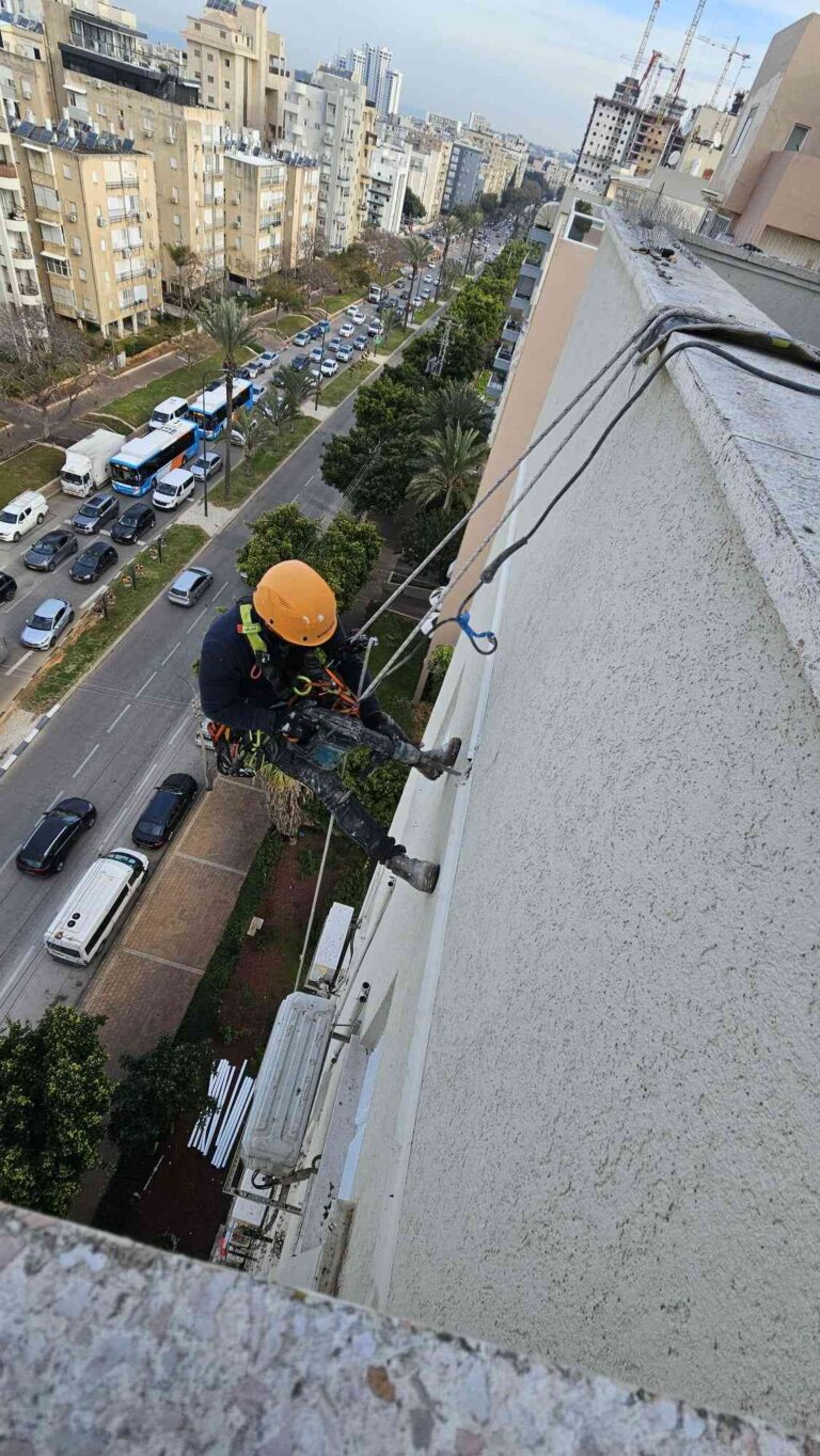 עובד מבצע עבודת סנפלינג בגובה על קיר חיצוני של בניין לצורך תיקון ותחזוקה.