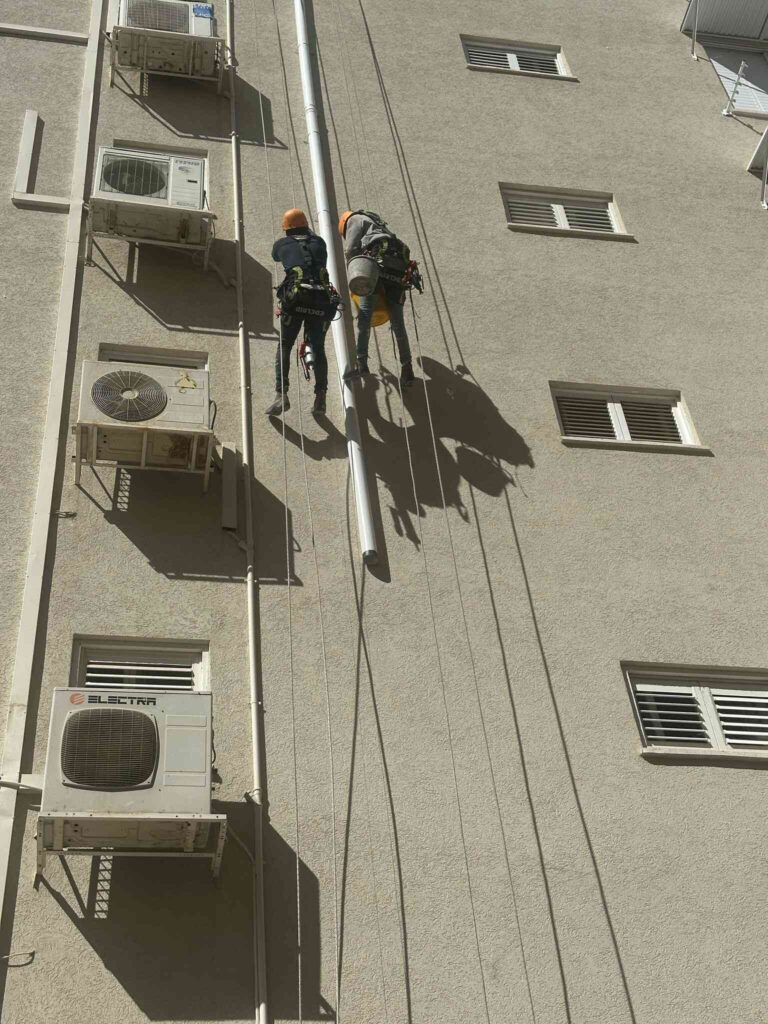 צוות עובדים מבצע עבודות סנפלינג בגובה על חזית בניין לצורך תחזוקה ותיקונים.