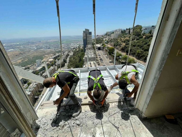 צוות עובדים מבצע עבודות תחזוקה ותיקון מרפסת באמצעות סנפלינג בגובה.